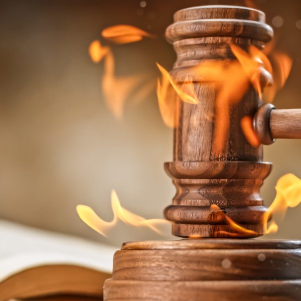 Burning wooden gavel with open law book on table.